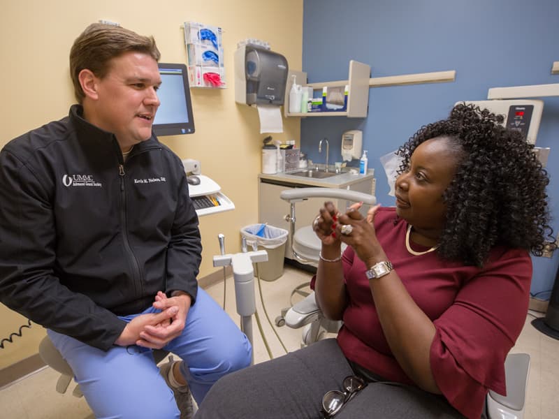 Patient speaking to doctor sitting on the edge of a desk.